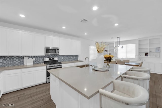 kitchen featuring appliances with stainless steel finishes, a sink, wood finished floors, a kitchen island with sink, and white cabinets