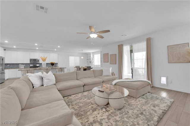 living area featuring a ceiling fan, recessed lighting, light wood-type flooring, and baseboards