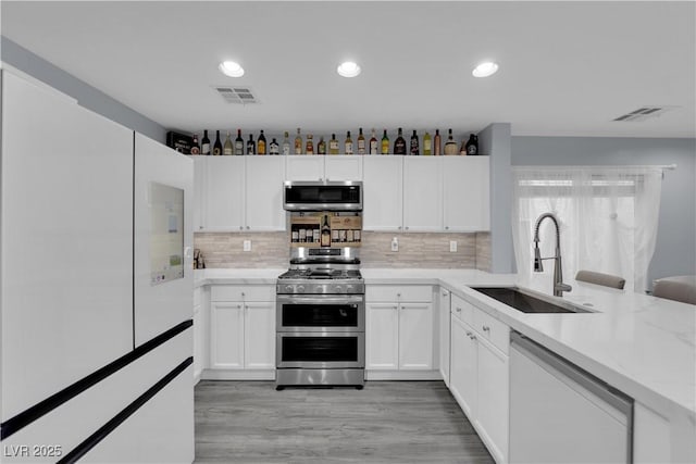9141 Careful Canvas Ave, Las Vegas, NV 89149 - kitchen with a sink, appliances with stainless steel finishes, white cabinetry, decorative backsplash, and light wood-style floors