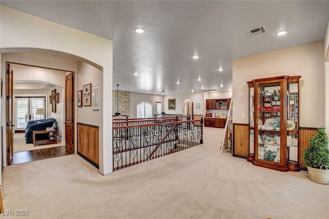 1182 Thomas Bay Cir, Logandale, NV 89021 - hallway featuring an upstairs landing, arched walkways, carpet flooring, a wainscoted wall, and plenty of natural light