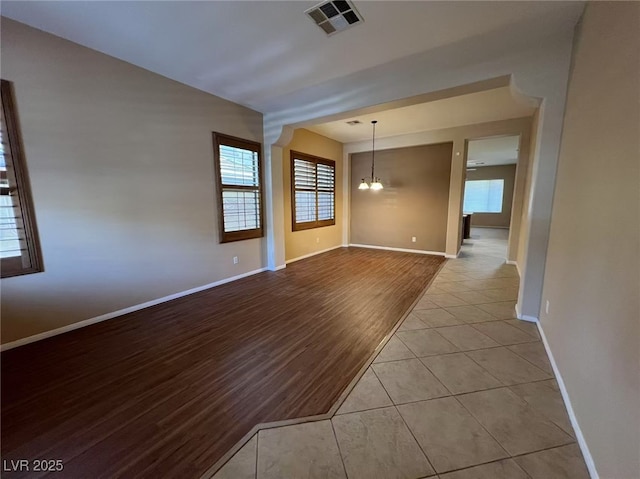 unfurnished room featuring a chandelier, healthy amount of natural light, baseboards, and wood finished floors