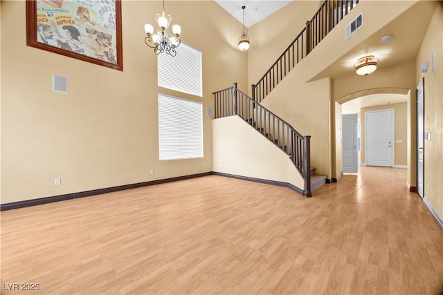 6088 Gulf Island Ave, Las Vegas, NV 89156 - unfurnished living room with light wood finished floors, arched walkways, baseboards, a chandelier, and a high ceiling