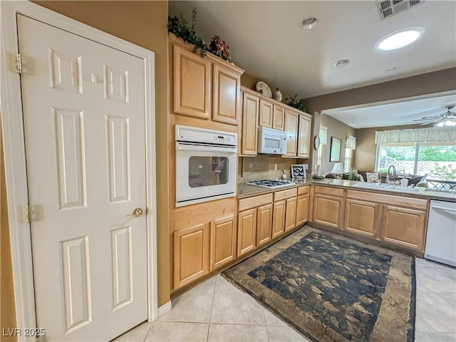 kitchen with white appliances, a sink, light brown cabinetry, and light tile patterned floors