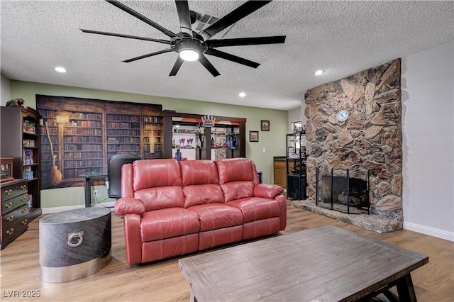 living room featuring a textured ceiling, ceiling fan, wood finished floors, a fireplace, and baseboards