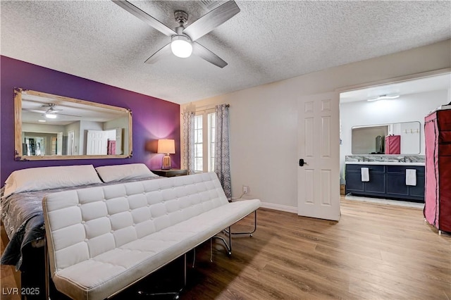 bedroom featuring wood finished floors, a textured ceiling, baseboards, ensuite bathroom, and a ceiling fan