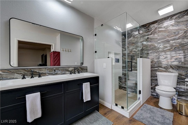 bathroom with wood finished floors, a shower stall, double vanity, and toilet