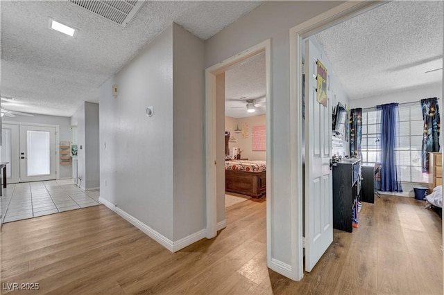 hall featuring a textured ceiling, light wood-type flooring, and baseboards
