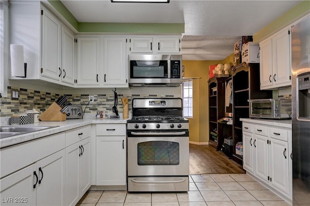 kitchen featuring appliances with stainless steel finishes, light countertops, white cabinetry, backsplash, and light tile patterned flooring