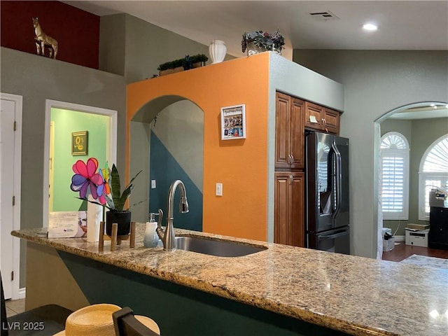 1800 Quail Point Ct, Las Vegas, NV 89117 - kitchen featuring black refrigerator with ice dispenser, a sink, brown cabinetry, arched walkways, and light stone counters