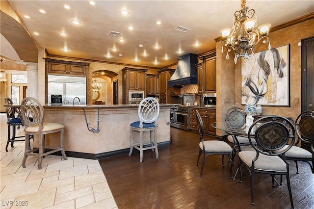 7625 Coley Ave, Las Vegas, NV 89117 - kitchen with custom exhaust hood, built in appliances, a breakfast bar area, a chandelier, and arched walkways