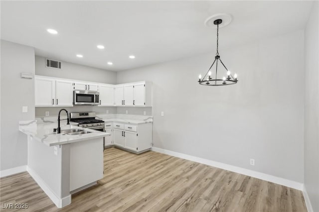2201 Ramsgate Dr Unit 327, Henderson, NV 89074 - kitchen with stainless steel appliances, a peninsula, a chandelier, baseboards, and light wood-style floors