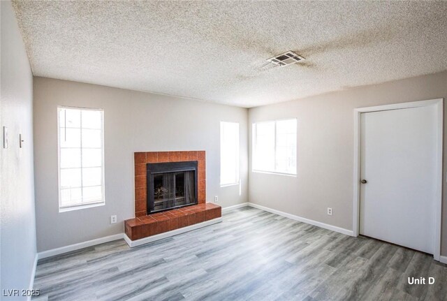 2755 Jennydiane Dr, Las Vegas, NV 89121 - unfurnished living room with wood finished floors, plenty of natural light, a tiled fireplace, a textured ceiling, and baseboards