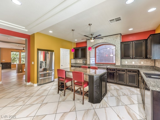 6779 Goose Watch Ct, Las Vegas, NV 89139 - kitchen with stainless steel refrigerator with ice dispenser, ceiling fan, a kitchen island, tasteful backsplash, and stone countertops