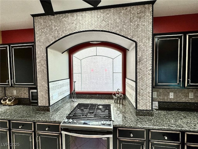 6779 Goose Watch Ct, Las Vegas, NV 89139 - kitchen with stainless steel gas range oven, dark cabinets, decorative backsplash, and dark stone countertops