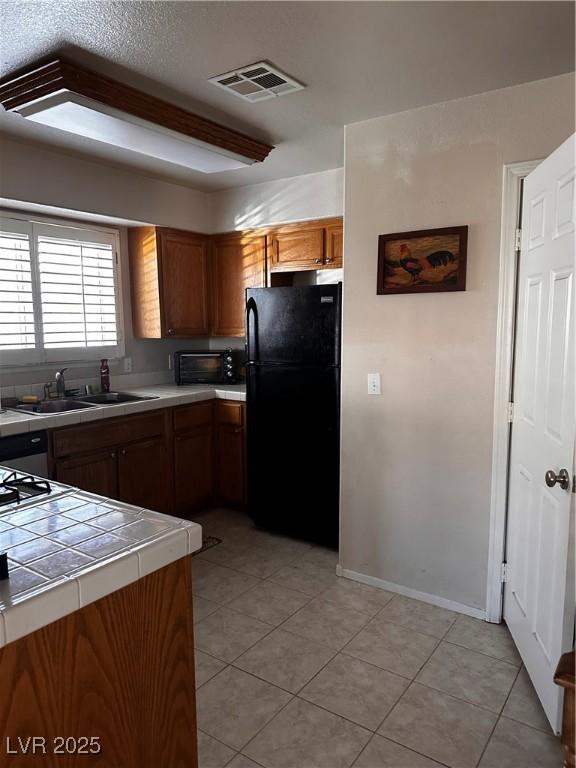 5020 Wildroot Rd, Las Vegas, NV 89130 - kitchen featuring freestanding refrigerator, tile counters, brown cabinets, and light tile patterned floors