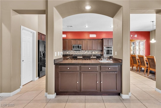 9362 Wilderness Glen Ave, Las Vegas, NV 89178 - kitchen featuring stainless steel microwave, black refrigerator with ice dispenser, dark countertops, arched walkways, and light tile patterned flooring