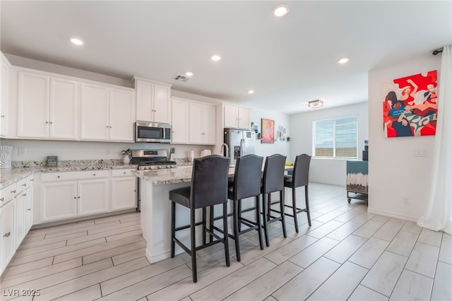7107 Calvert Cliffs St, North Las Vegas, NV 89084 - kitchen with appliances with stainless steel finishes, white cabinetry, a kitchen breakfast bar, a center island, and light stone countertops