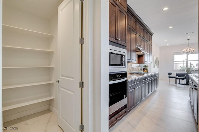 350 Gandara St, Las Vegas, NV 89138 - kitchen with appliances with stainless steel finishes, dark brown cabinetry, under cabinet range hood, a chandelier, and tasteful backsplash