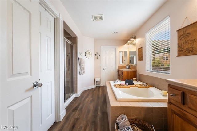bathroom featuring a shower stall, wood finished floors, a bath, vanity, and baseboards
