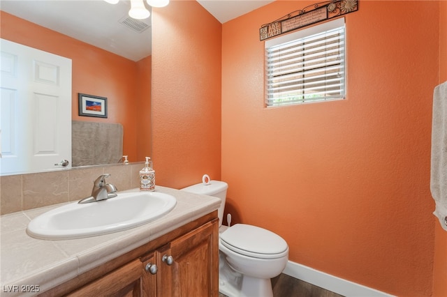 half bathroom with toilet, wood finished floors, a textured wall, vanity, and baseboards