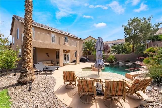 rear view of house featuring a balcony, stucco siding, a fenced backyard, french doors, and a patio area