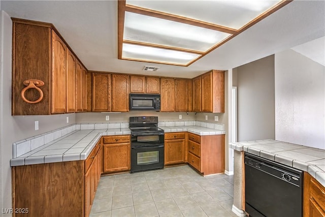 kitchen with black appliances, brown cabinets, light tile patterned flooring, and tile counters
