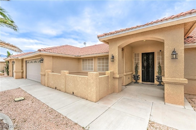 entrance to property with a tiled roof, stucco siding, a garage, and driveway