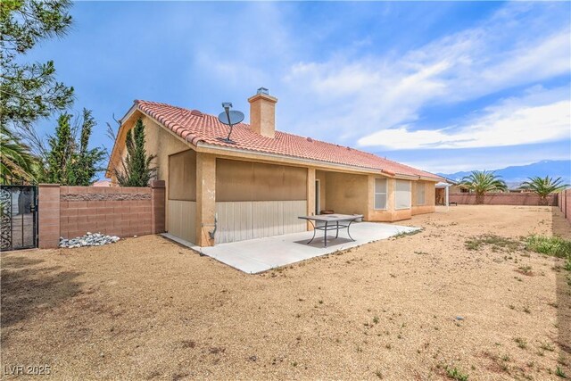 rear view of house featuring a chimney, a tiled roof, a patio, a fenced backyard, and a gate