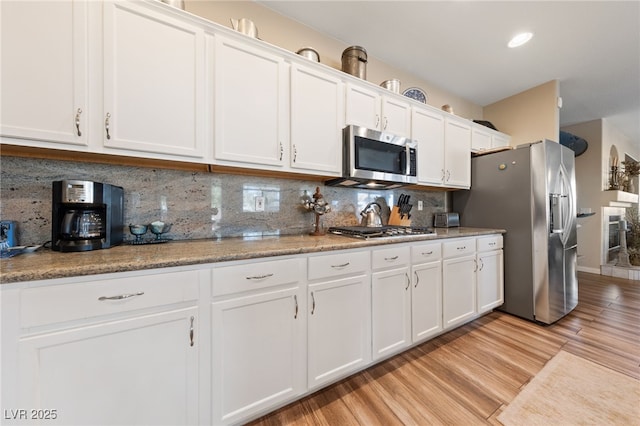 6999 Stone Meadows Ave, Las Vegas, NV 89142 - kitchen featuring appliances with stainless steel finishes, white cabinetry, light wood-type flooring, and tasteful backsplash