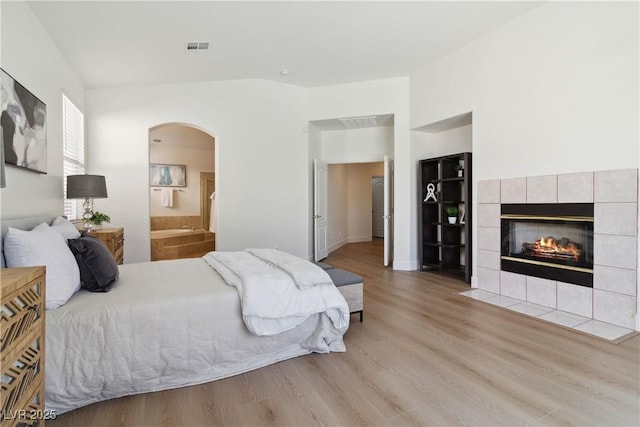 8714 Las Posas Ave, Las Vegas, NV 89147 - bedroom featuring arched walkways, light wood finished floors, a tiled fireplace, and ensuite bath