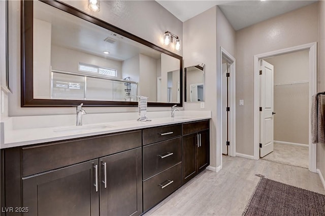 2902 Ventana Ridge Ave, Henderson, NV 89044 - bathroom featuring a shower with door, wood finished floors, double vanity, a walk in closet, and baseboards