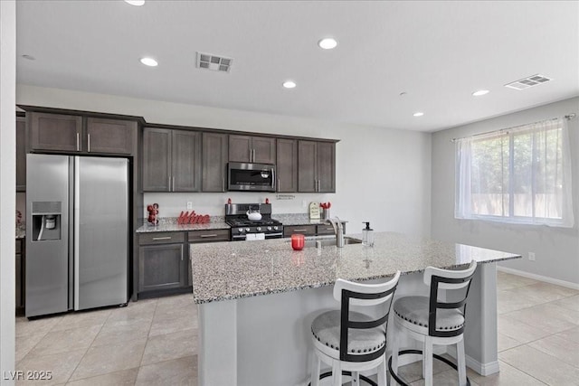 2276 Sky Island Dr, Henderson, NV 89002 - kitchen featuring appliances with stainless steel finishes, light stone countertops, light tile patterned flooring, dark brown cabinetry, and a breakfast bar area