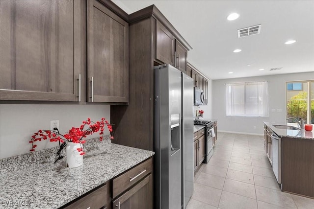 2276 Sky Island Dr, Henderson, NV 89002 - kitchen featuring stainless steel appliances, light stone countertops, dark brown cabinetry, recessed lighting, and light tile patterned flooring
