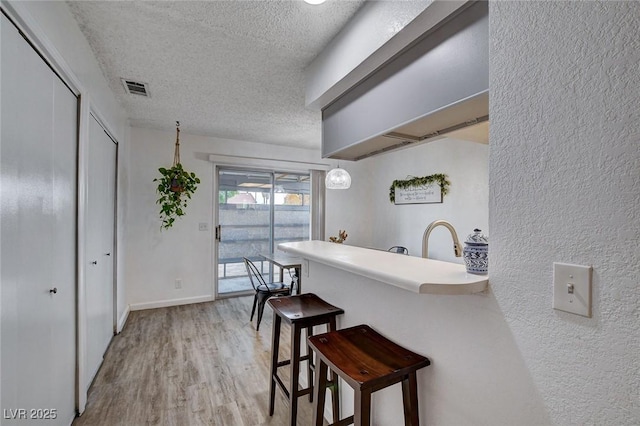 227 N Lamb Blvd Unit B, Las Vegas, NV 89110 - kitchen with a textured ceiling, a breakfast bar, light wood-style flooring, a textured wall, and light countertops