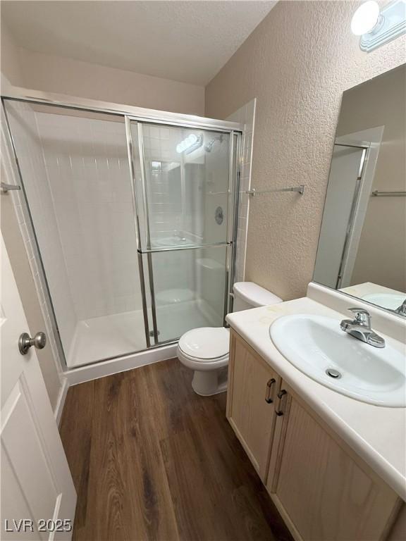 7969 Cina Ave, Las Vegas, NV 89147 - bathroom featuring a textured wall, wood finished floors, a shower stall, toilet, and vanity