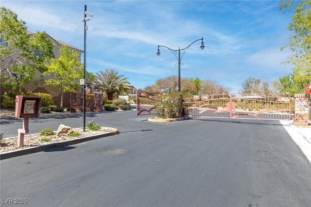 7641 Lani Dawn St, Las Vegas, NV 89149 - view of asphalt road with a gate, curbs, a gated entry, and street lights