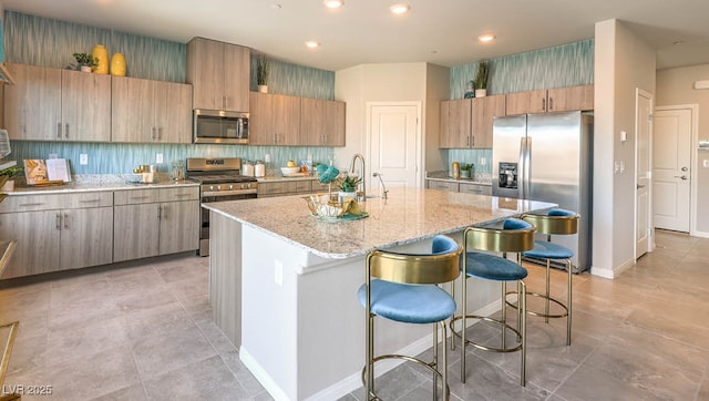 kitchen featuring stainless steel appliances, a sink, light stone counters, a kitchen breakfast bar, and a center island with sink