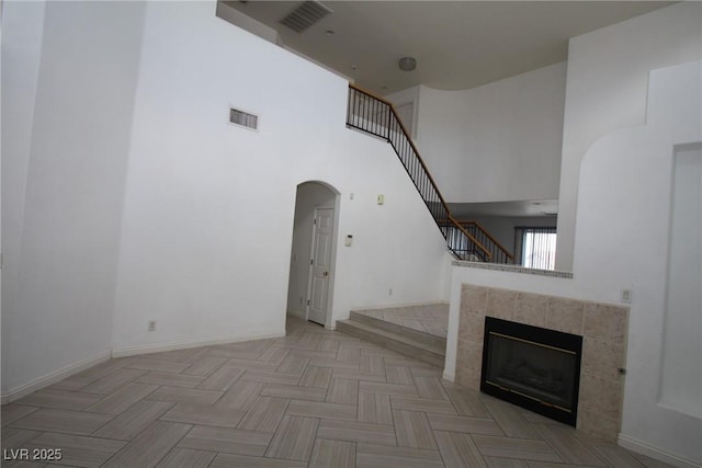 3440 Crystal Tower St, Las Vegas, NV 89129 - unfurnished living room with arched walkways, a high ceiling, stairs, a tile fireplace, and baseboards