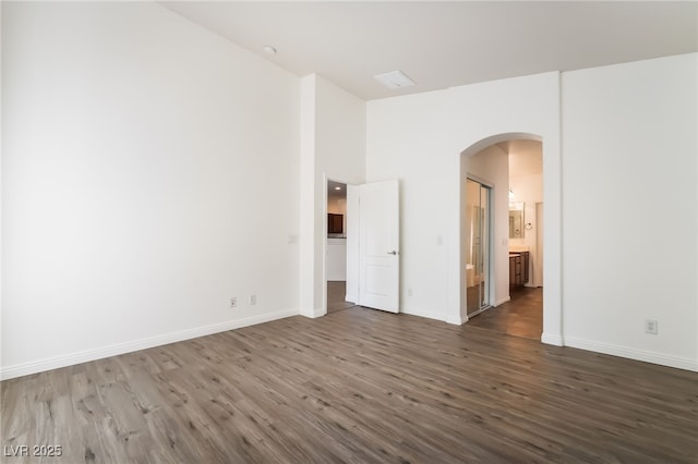 spare room with arched walkways, dark wood-style floors, and baseboards