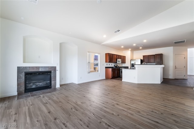 unfurnished living room featuring lofted ceiling, dark wood-style floors, a tile fireplace, recessed lighting, and baseboards