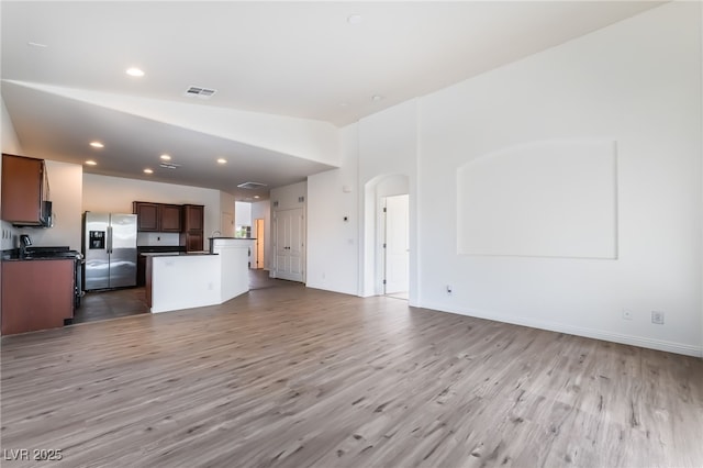 unfurnished living room featuring light wood finished floors, arched walkways, recessed lighting, baseboards, and vaulted ceiling