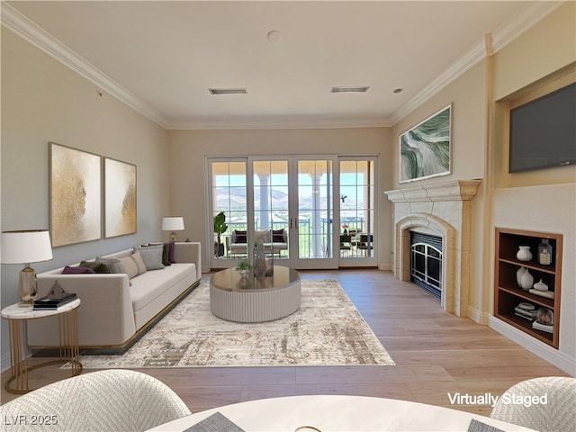 living room featuring crown molding, light wood-style floors, a glass covered fireplace, and built in shelves