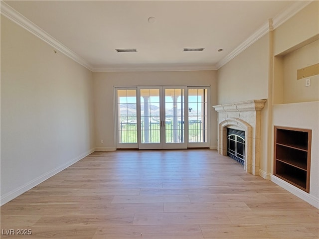 unfurnished living room with ornamental molding, light wood-style flooring, a premium fireplace, baseboards, and french doors