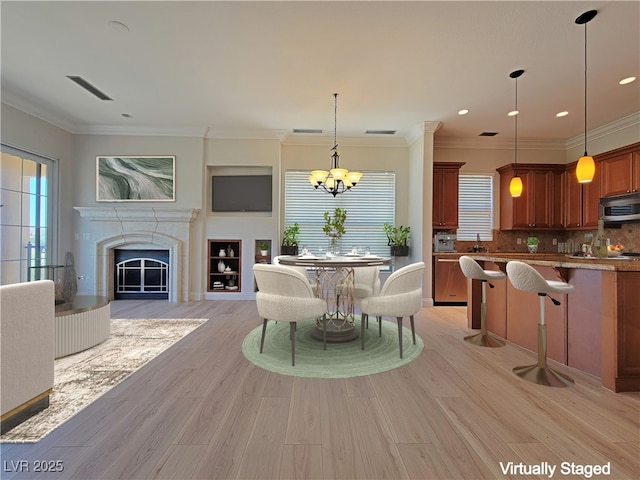 dining room with a chandelier, a fireplace, light wood-style flooring, ornamental molding, and recessed lighting