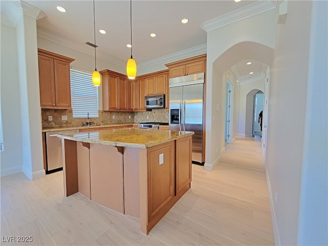 kitchen with appliances with stainless steel finishes, arched walkways, a sink, a kitchen island, and backsplash