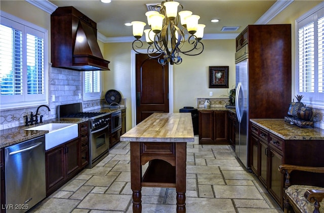 kitchen featuring built in appliances, wooden counters, a sink, ornamental molding, and stone tile flooring