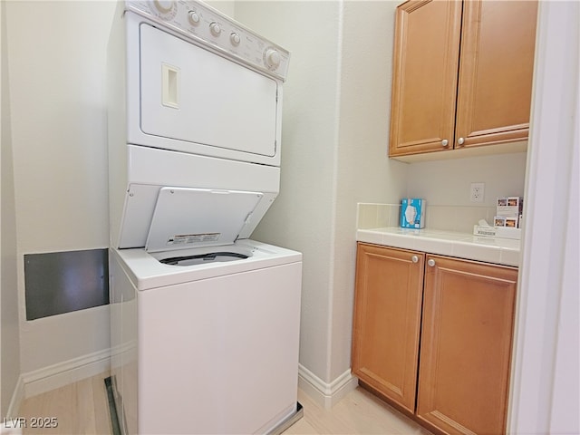 laundry room with estacked washer and dryer, cabinet space, and baseboards