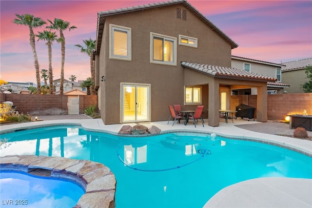 back of property at dusk with stucco siding, a tile roof, a fenced backyard, and a patio area