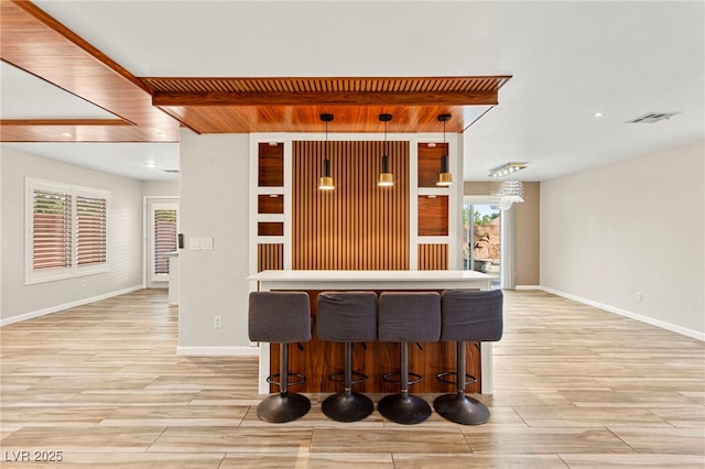 kitchen with light wood finished floors, baseboards, decorative light fixtures, a breakfast bar area, and open floor plan