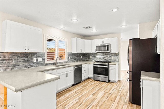 kitchen featuring stainless steel appliances, a peninsula, a sink, tasteful backsplash, and light countertops